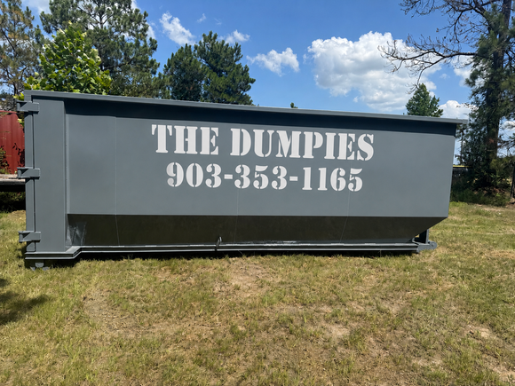 A large black dumpster is sitting on top of a dirt road.