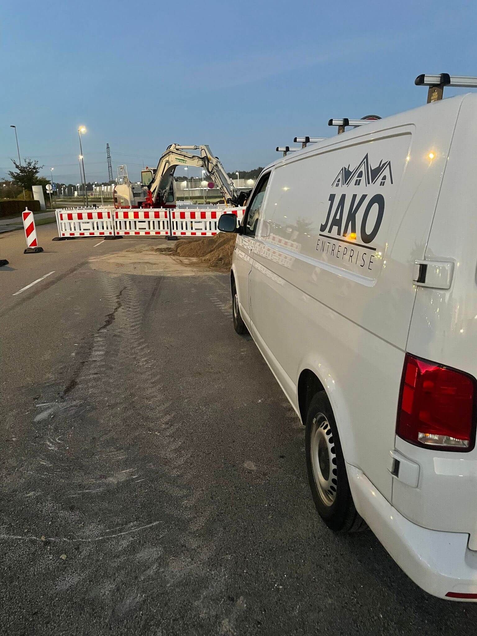 En hvid varevogn med ordet jako på siden er parkeret i siden af ​​vejen.