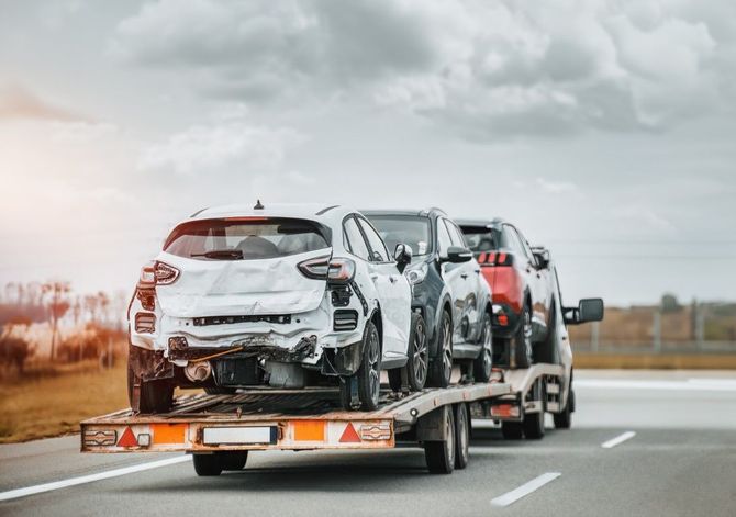 Car carrier trailer hauling wrecked cars on a highway under cloudy skies