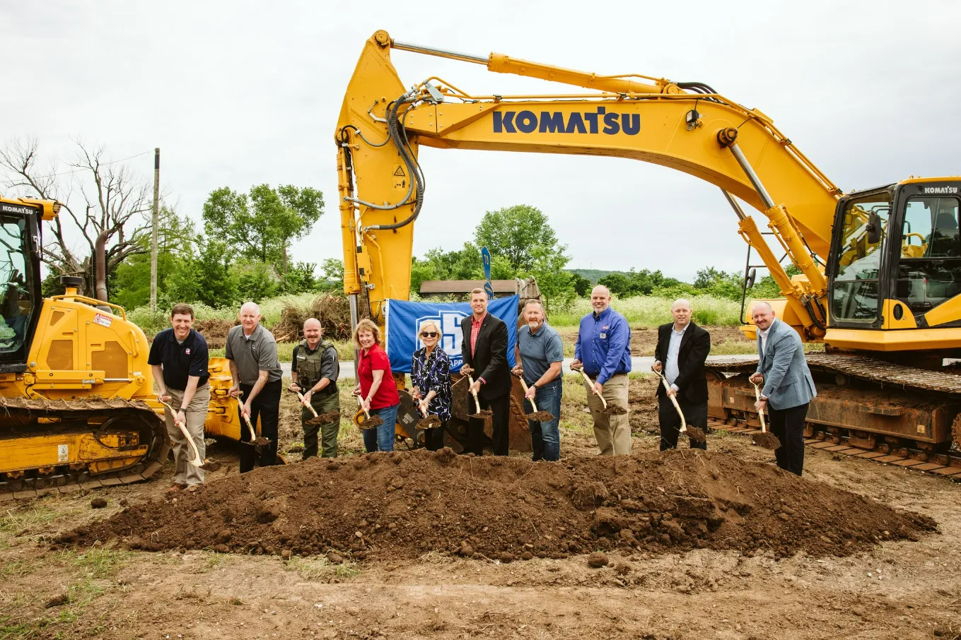 Group of people breaking ground with shovels for a new construction project, Komatsu excavator in background.
