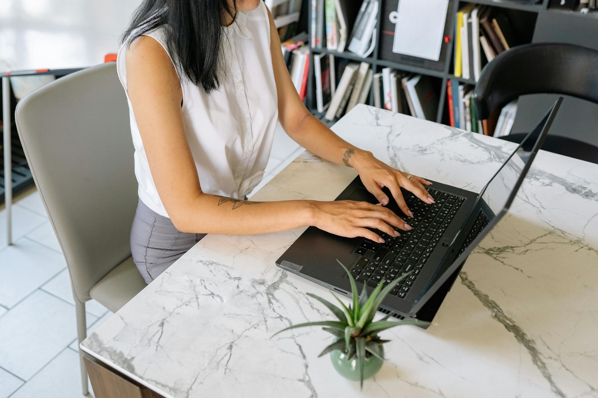 Person typing on a laptop at a marble table in a bright office setting