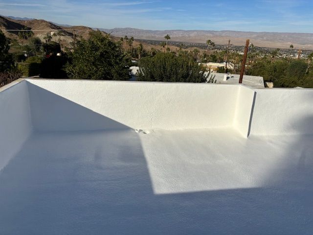White flat roof with a parapet, in a sunny setting with a mountain landscape in the background.
