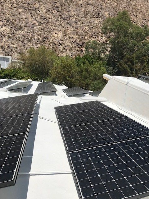 Solar panels on a white roof against a backdrop of a rocky hillside and green trees.