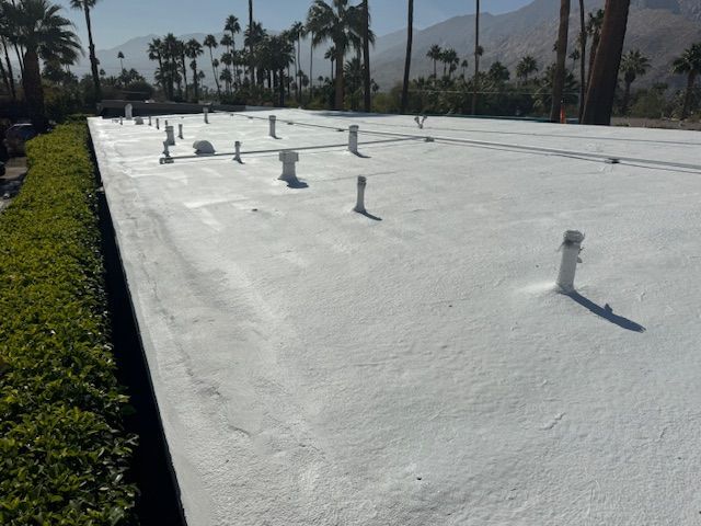Flat white roof with pipes extending upwards, palm trees and mountains in the background.