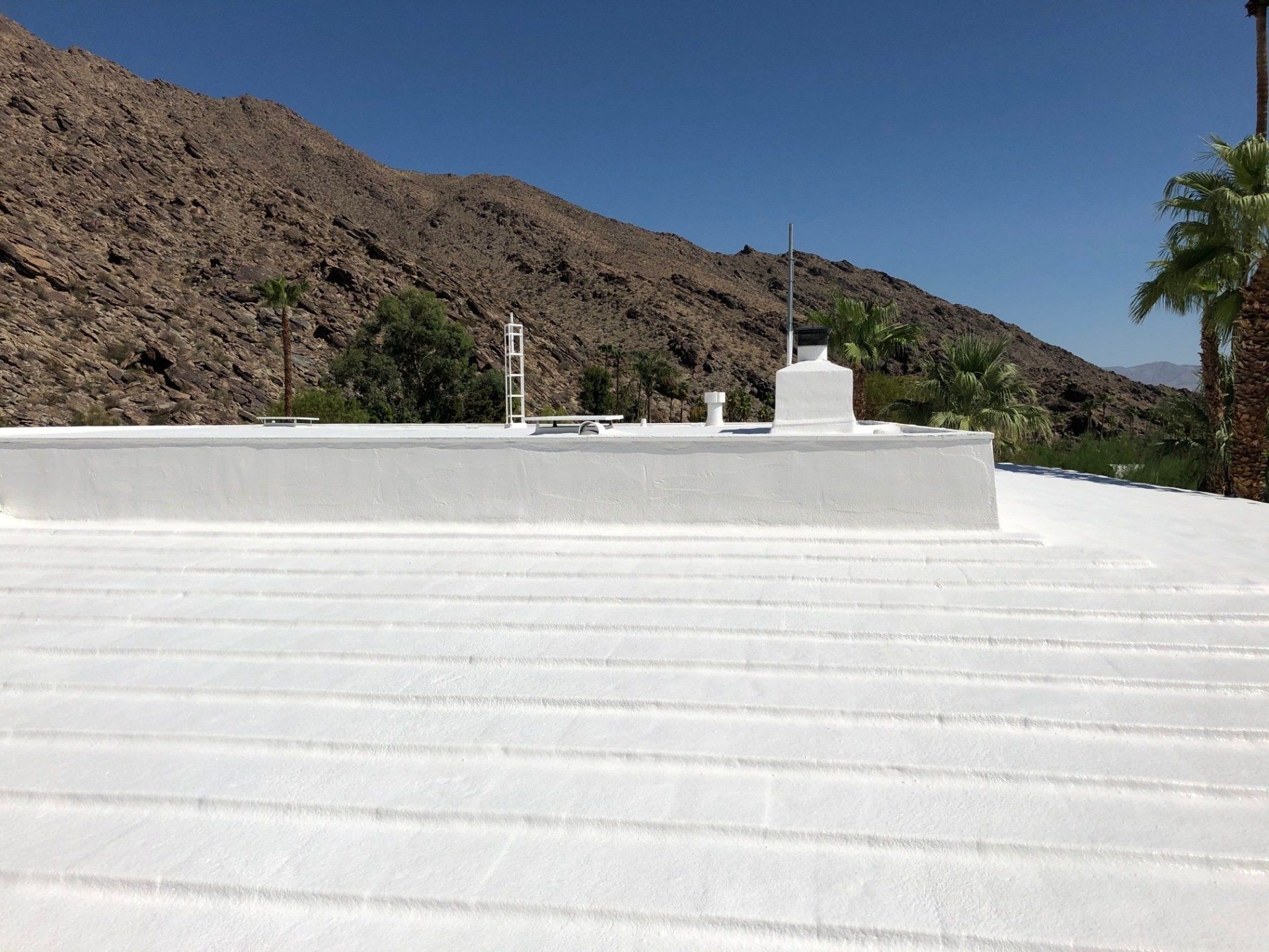 White roof with a mountain backdrop and blue sky. There are antennas and other equipment on the roof.