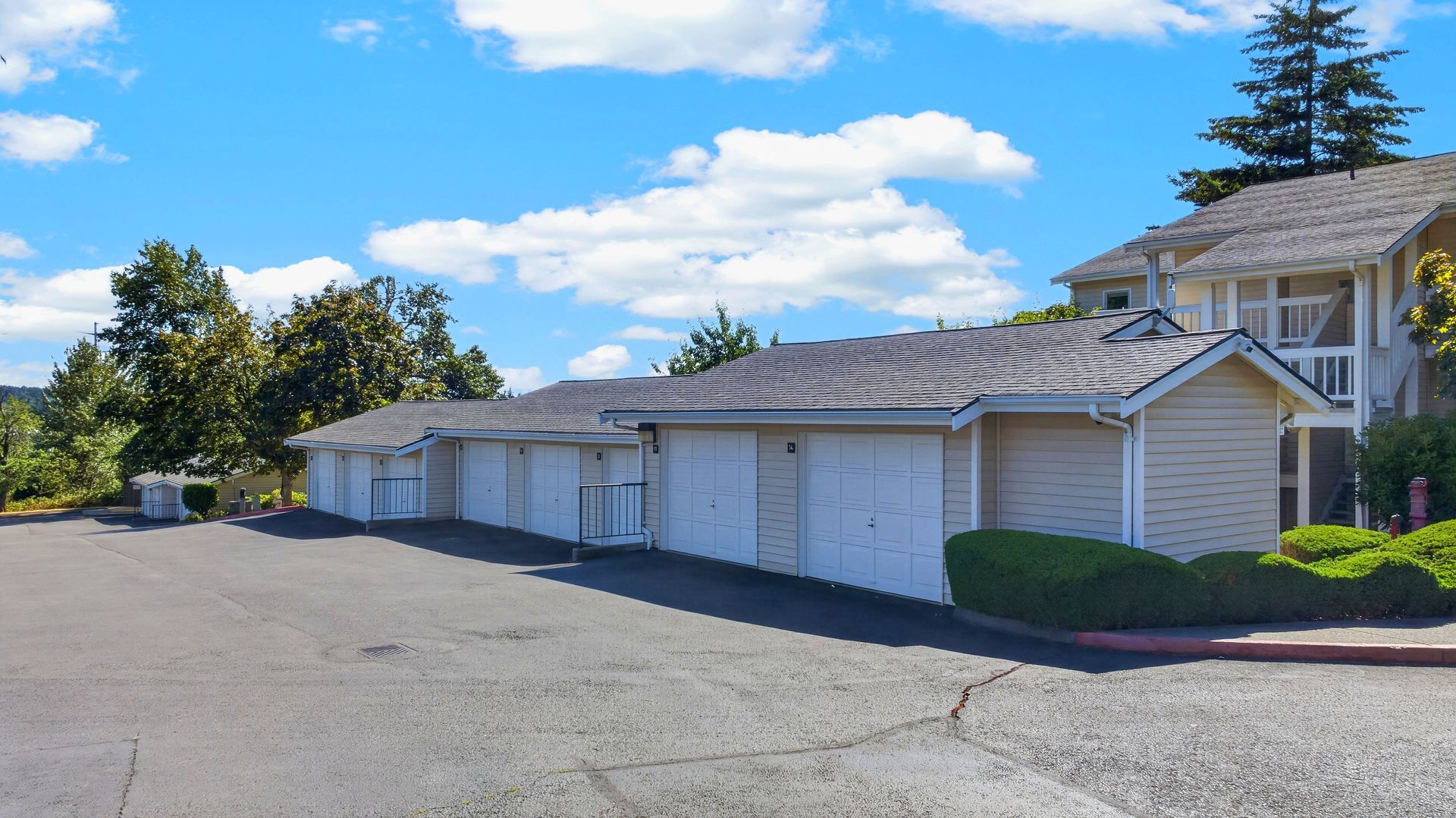 Row of white garage units beside a paved lot under a blue sky with clouds