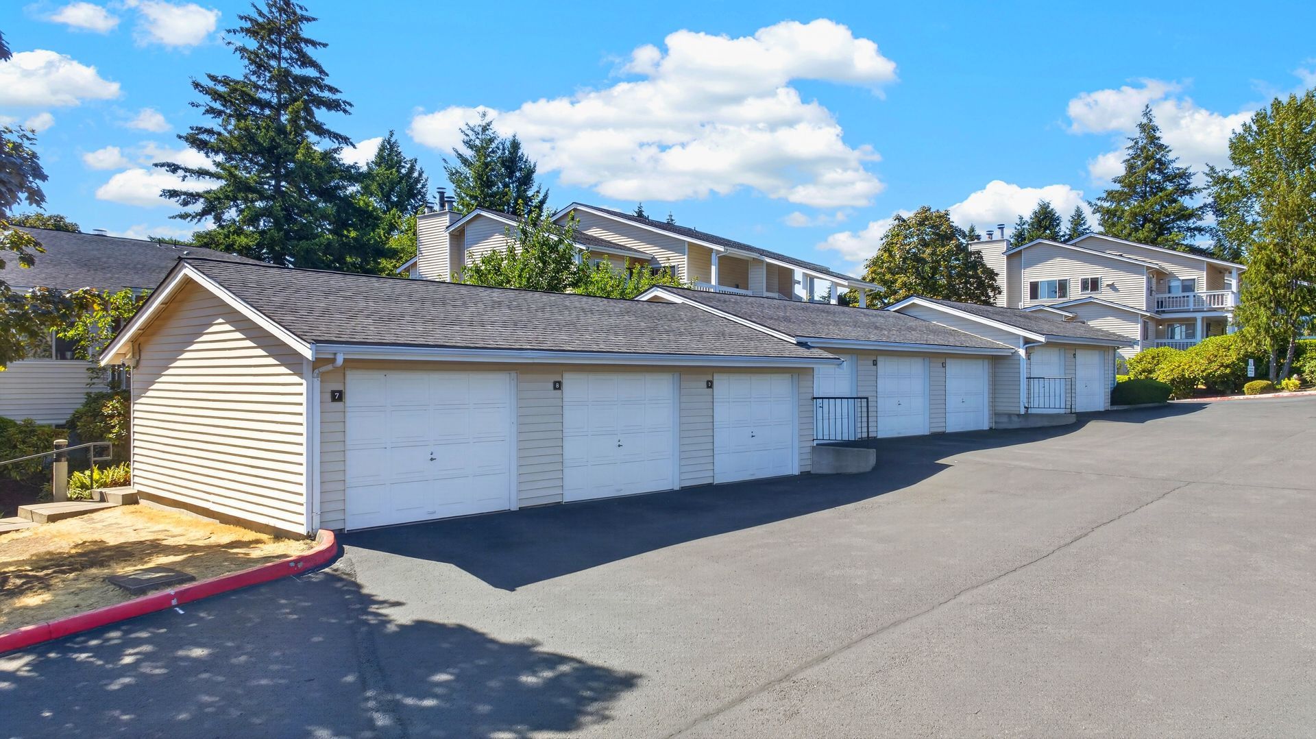 Row of beige garage units with white doors beside a paved lot under a blue sky