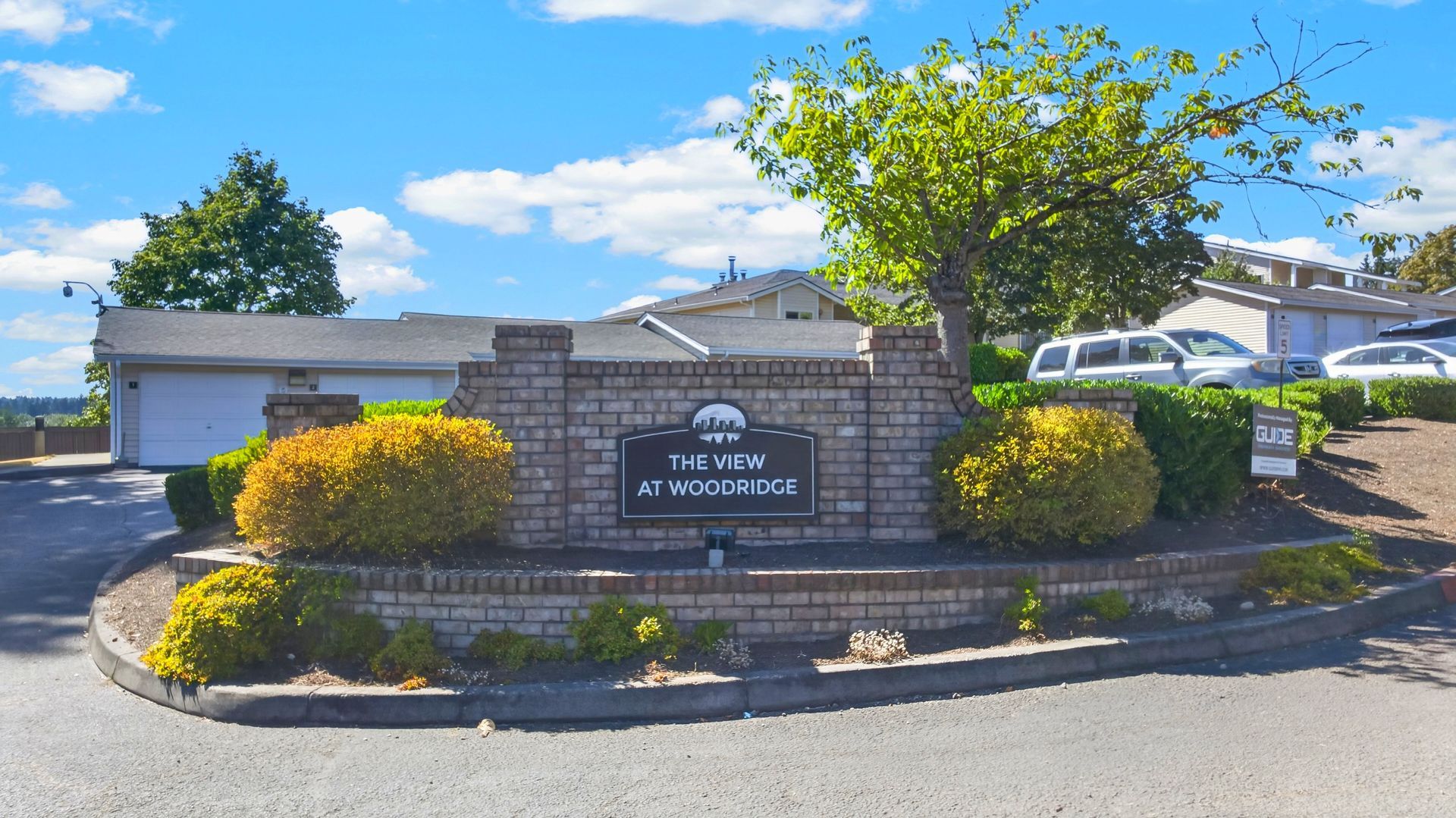 Stone sign for “The Pines” surrounded by shrubs at a sunny residential entrance