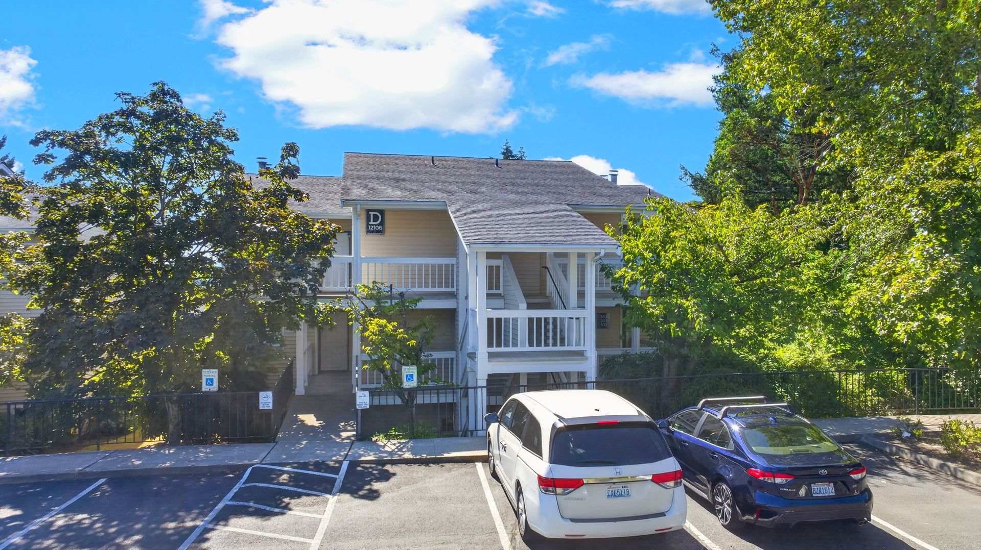 Apartment building with balconies and parked cars under a bright blue sky.