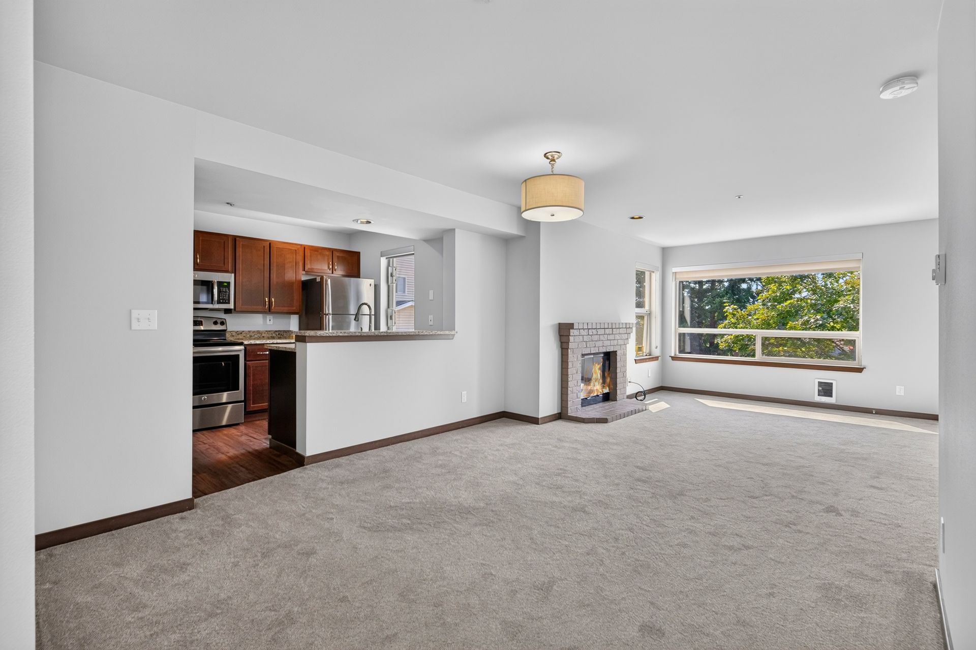 Bright empty living room with carpet, fireplace, open kitchen, and large window view