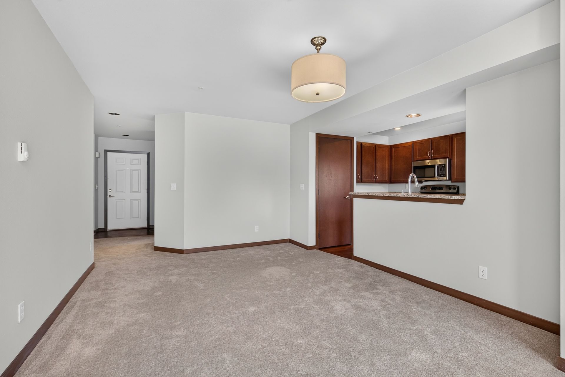 Empty carpeted living room with white walls and a kitchen pass-through in the background