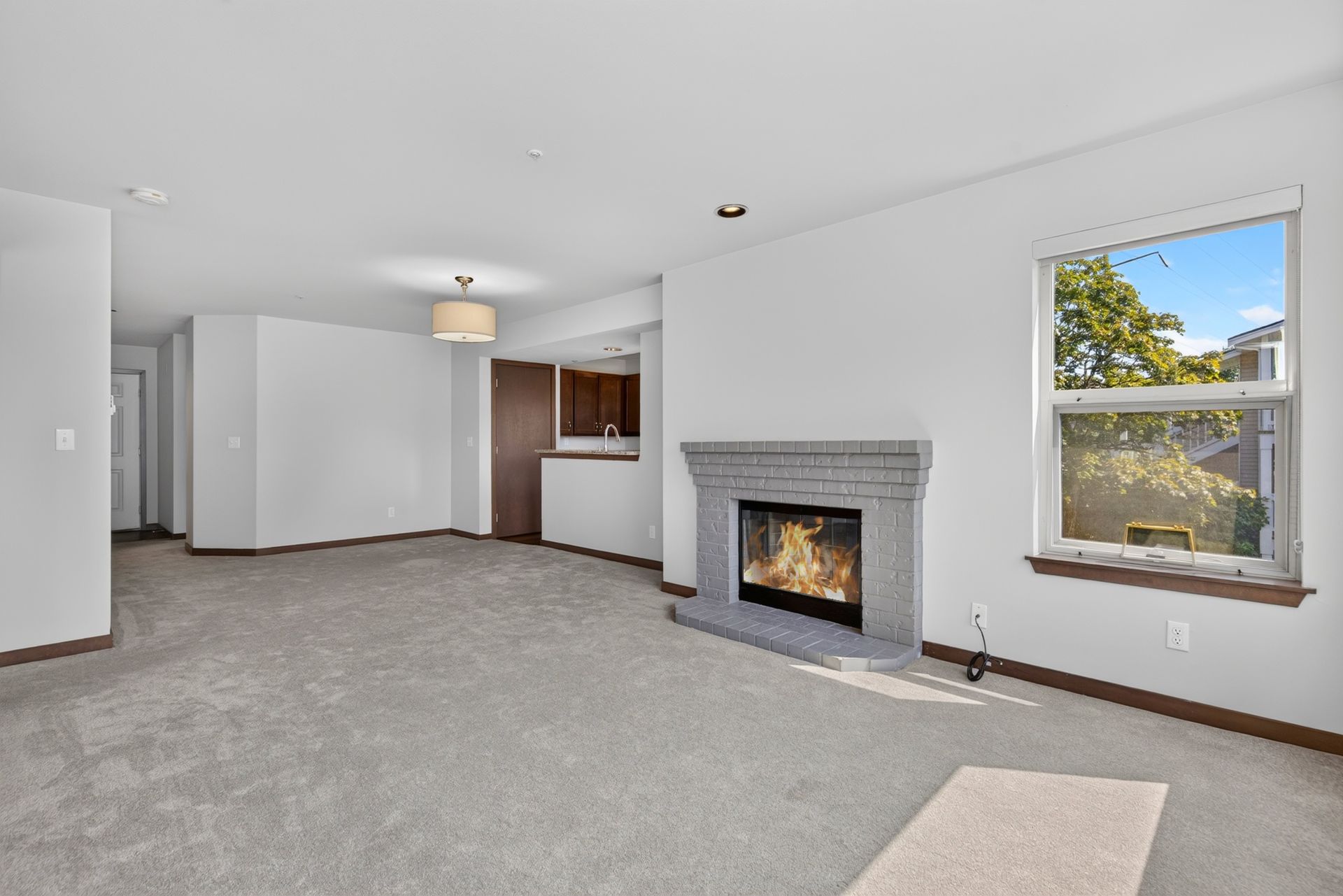 Empty living room with gray carpet, white walls, a fireplace, and a large window.