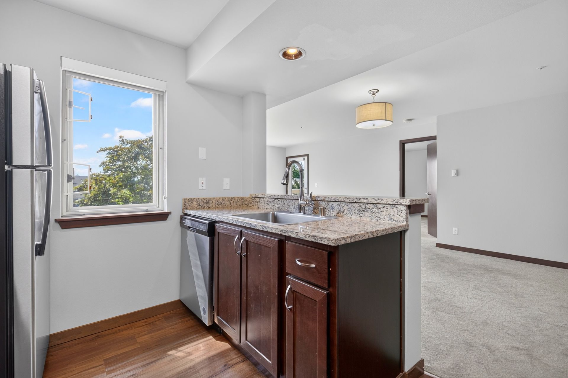 Bright kitchen nook with granite island, dark wood cabinets, window, and carpeted adjoining room