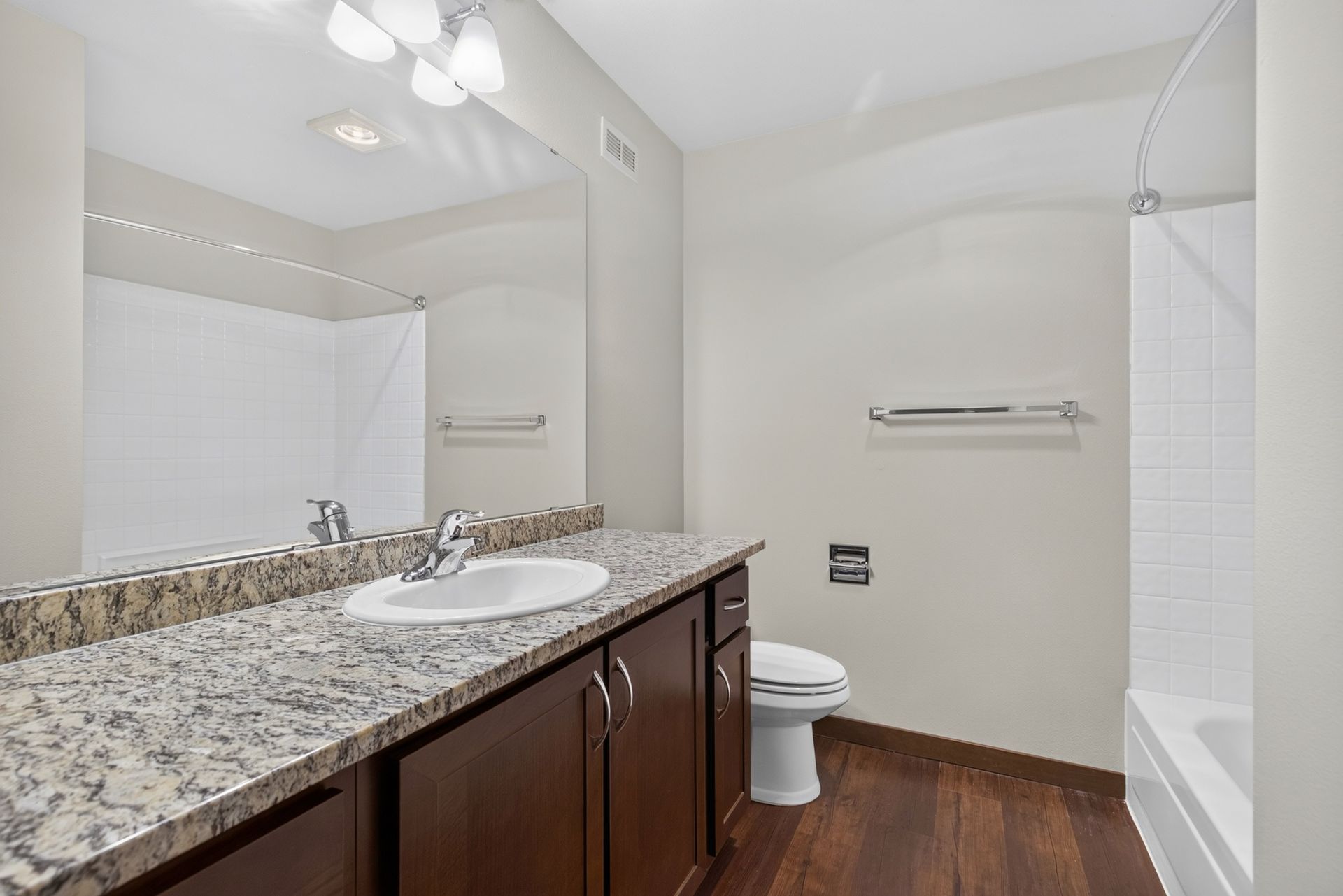 Modern bathroom with granite vanity, toilet, tub, white walls, and wood floor