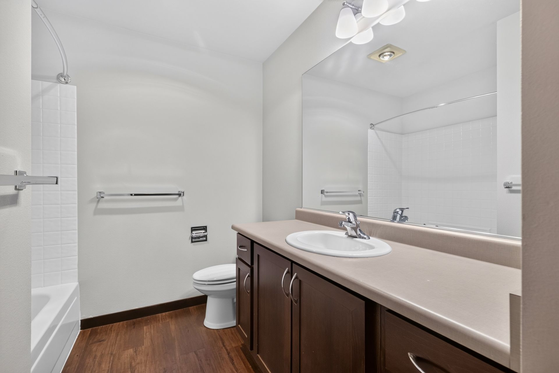 Bright bathroom with white walls, dark wood vanity, toilet, bathtub, and large mirror