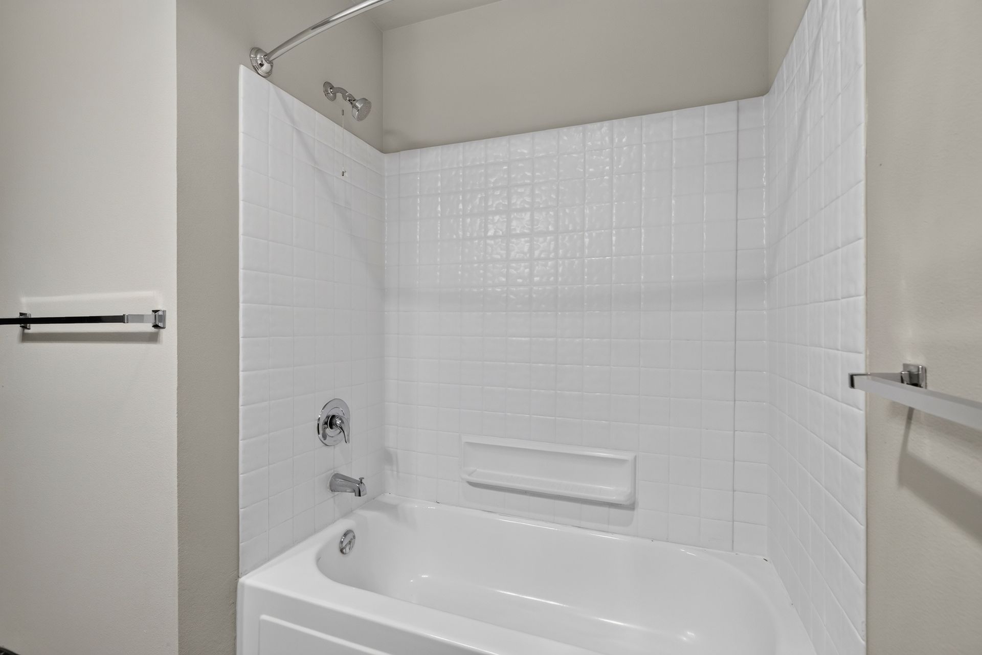 White tiled bathroom with a bathtub and shower area, plus towel bars on the walls