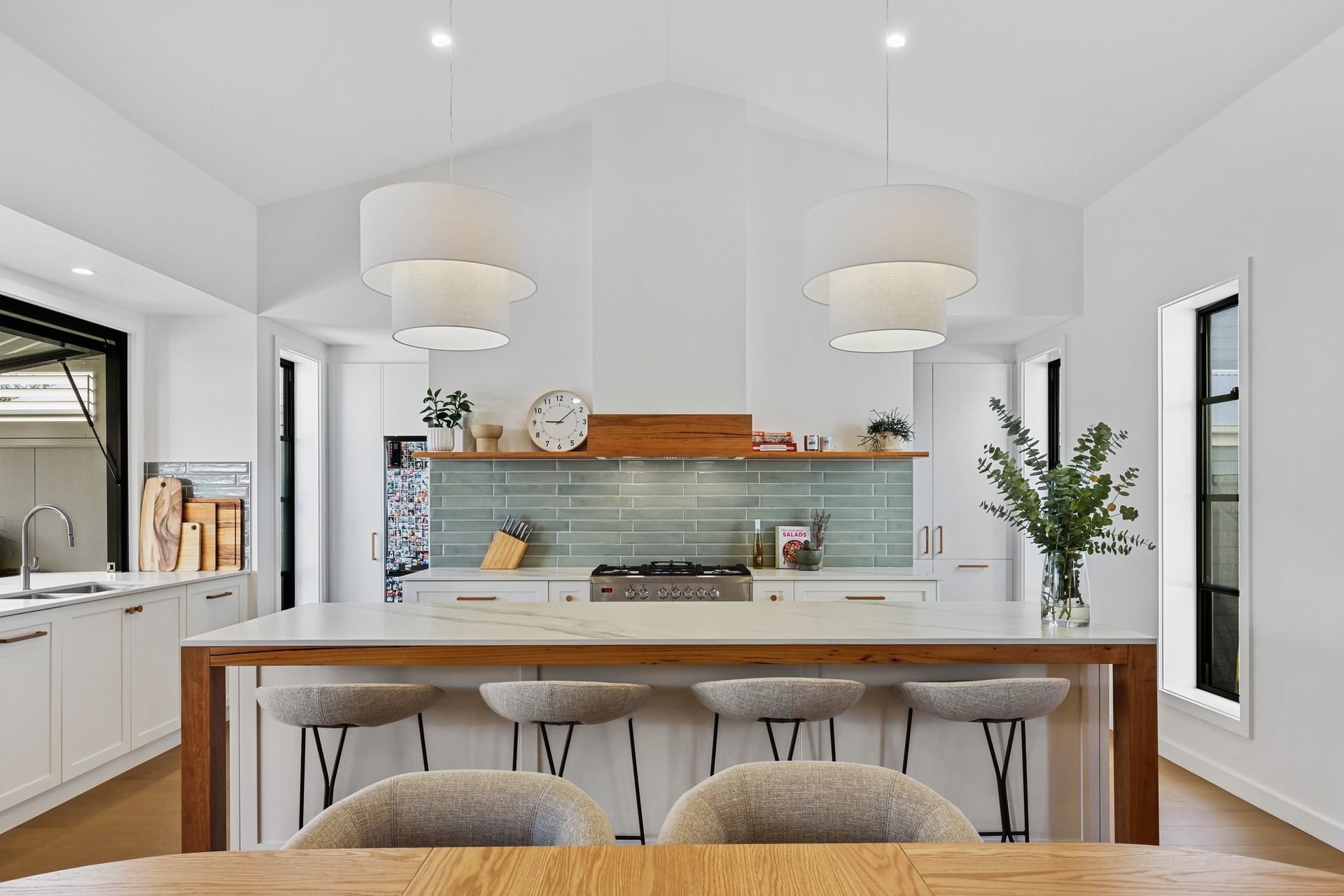 Kitchen with a timber benchtop edge, stools, pendant lights and a green tile splashback