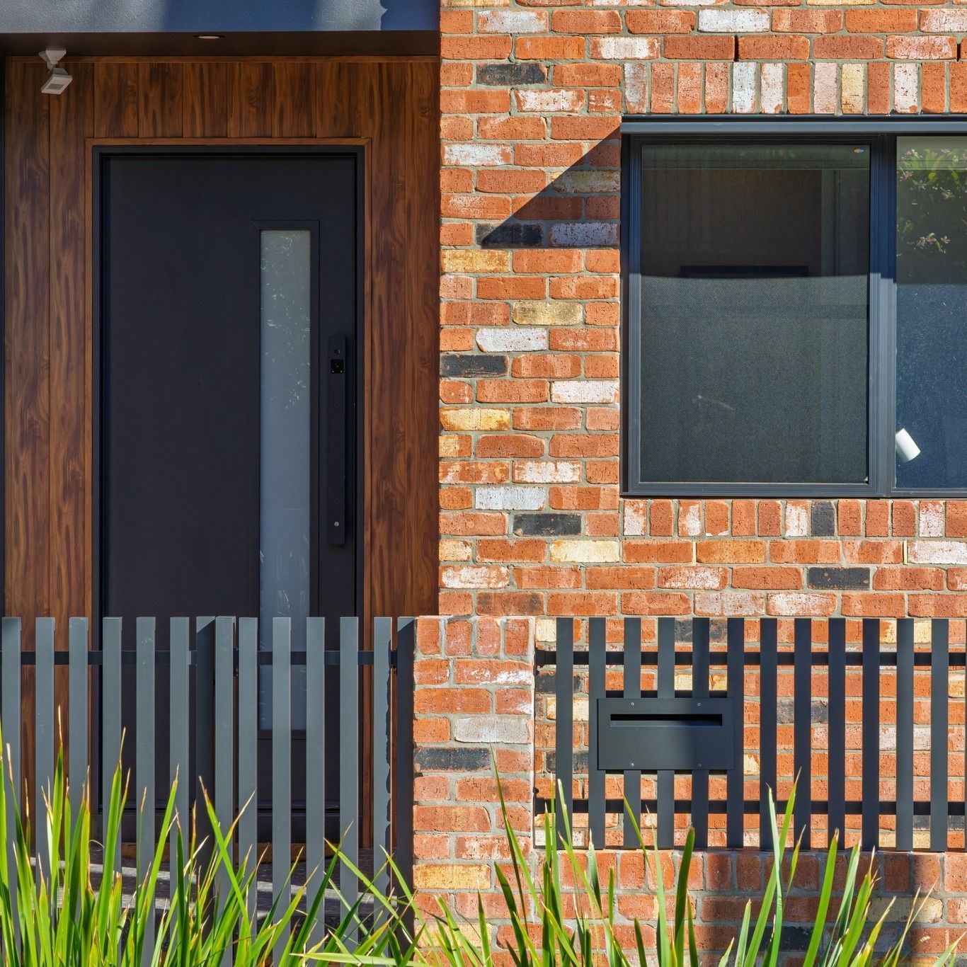 Front entry with a timber-look door, face brick and black picket fence on a custom home in Islington