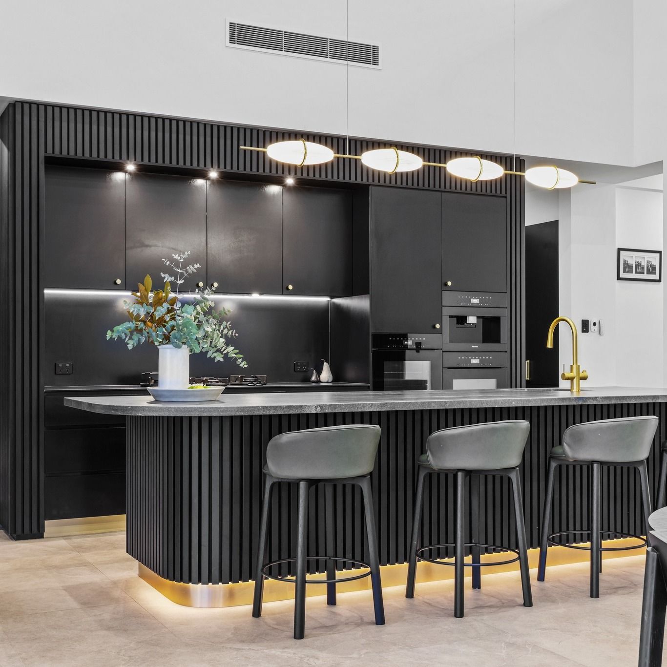 Kitchen with a black fluted island, three stools, pendant lights and black cabinetry