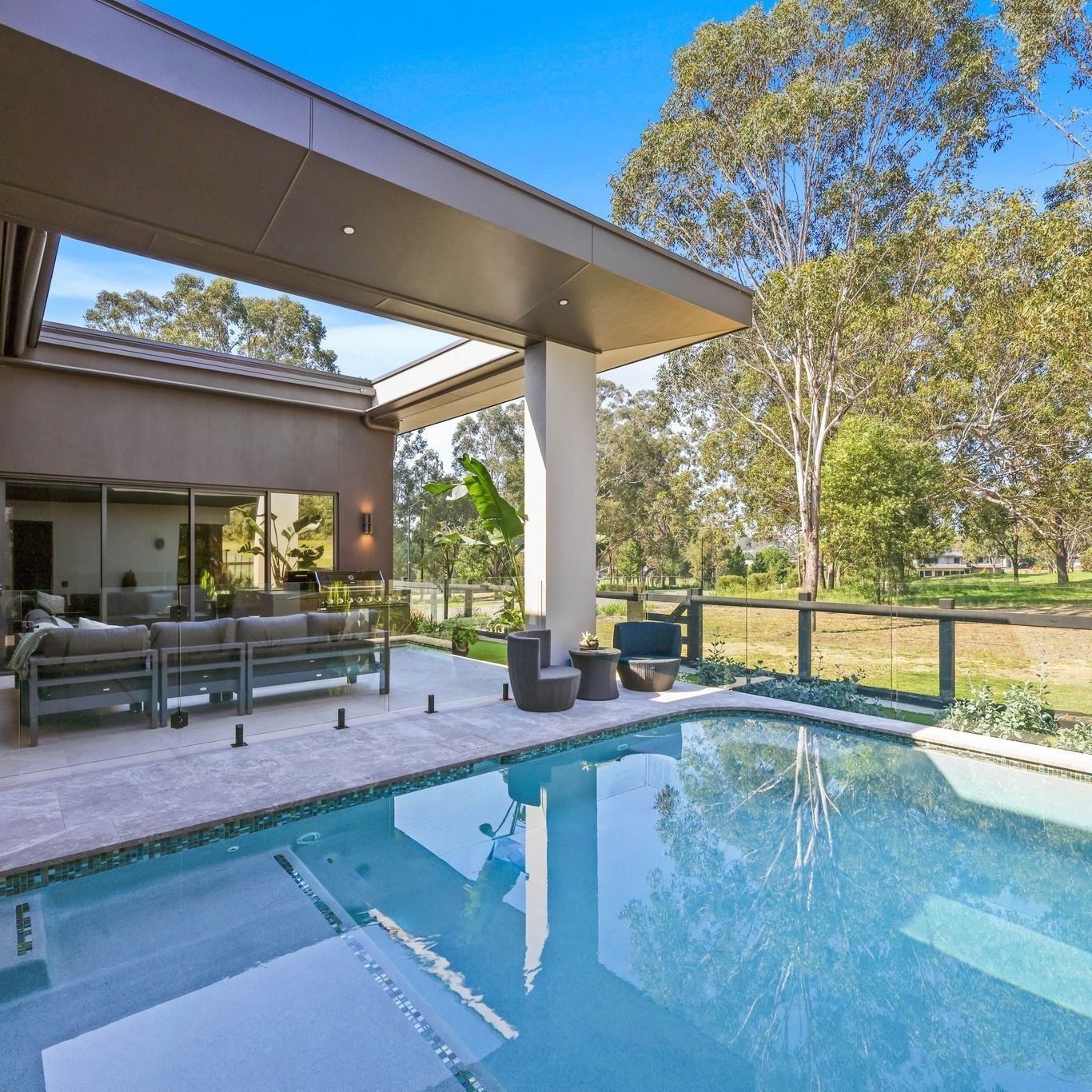 Covered outdoor living area with lounge seating beside a swimming pool