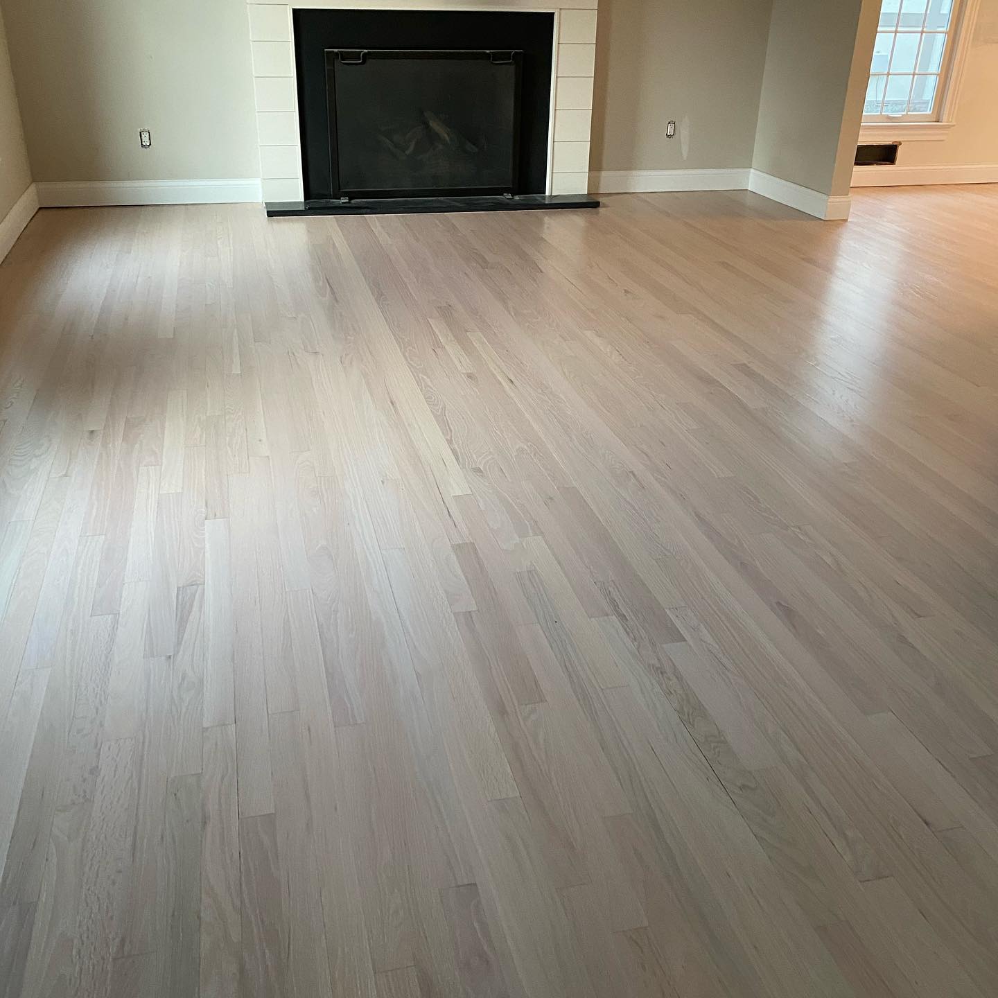 Empty living room with light wood floors and a black fireplace on the far wall