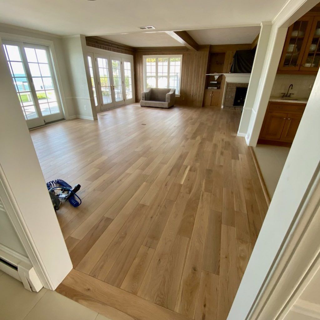 Spacious empty living room with light wood floors, large windows, and a fireplace.