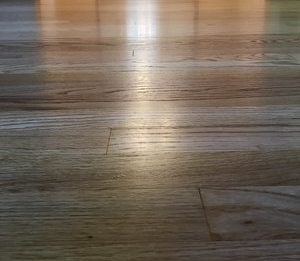 Close-up of a sunlit wooden floor with visible planks and reflections.