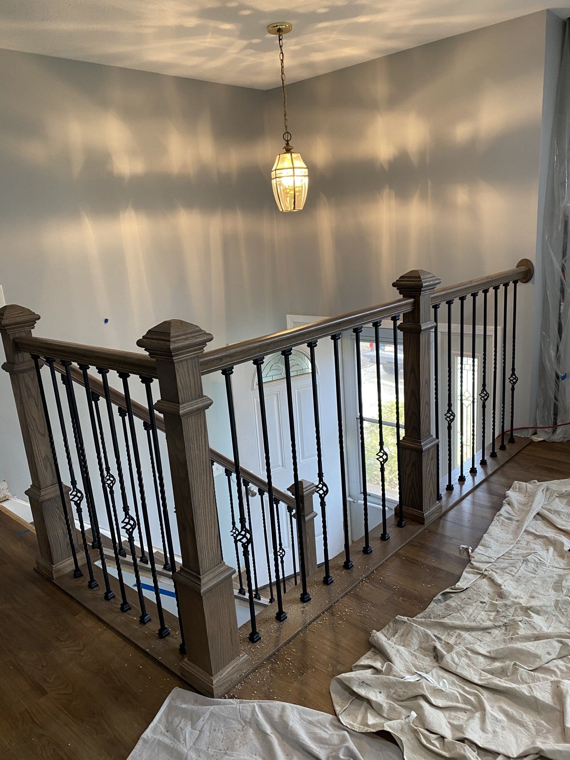 Stair landing with ornate dark railing, hanging pendant light, and white tarp-covered floor in a hallway
