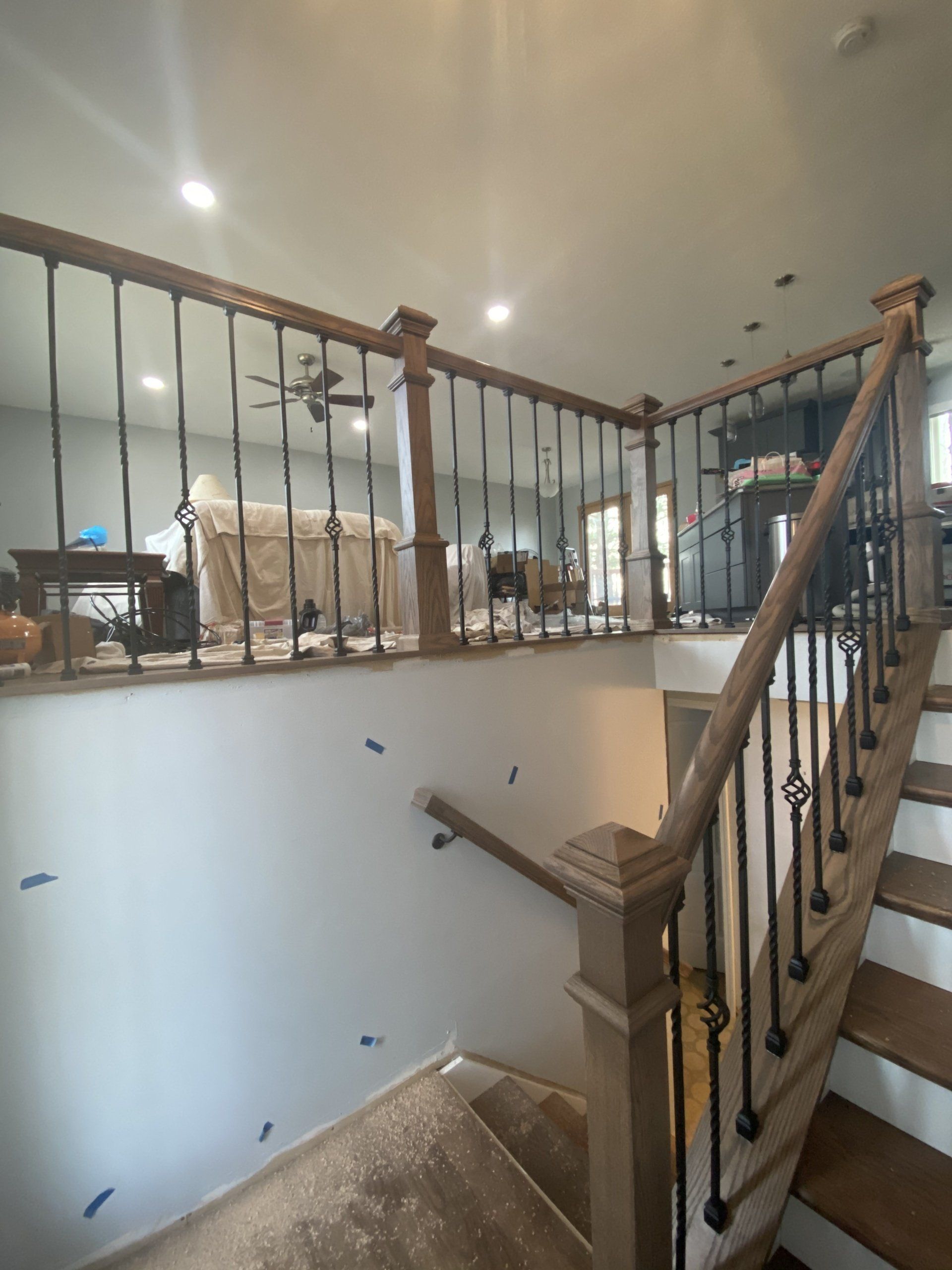 Staircase landing with wood railing, black iron balusters, and an open view into a bright living room.