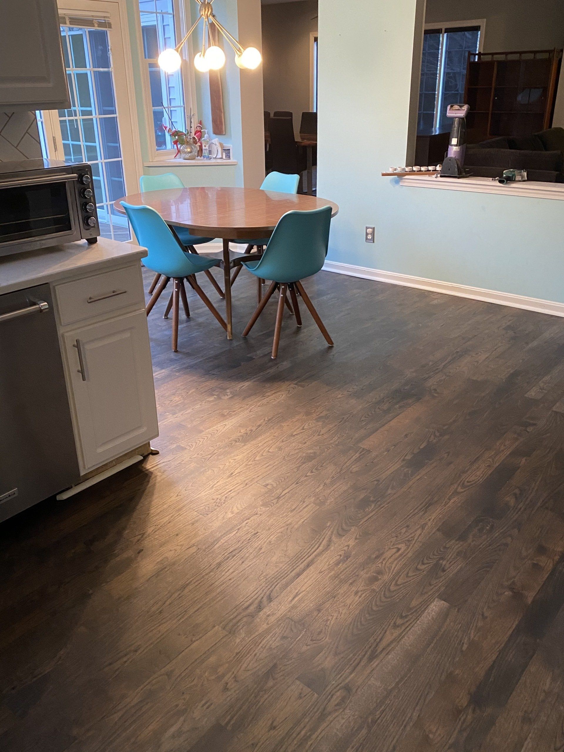 Empty kitchen with blue walls, dark wood floors, and a small round table with two teal chairs.