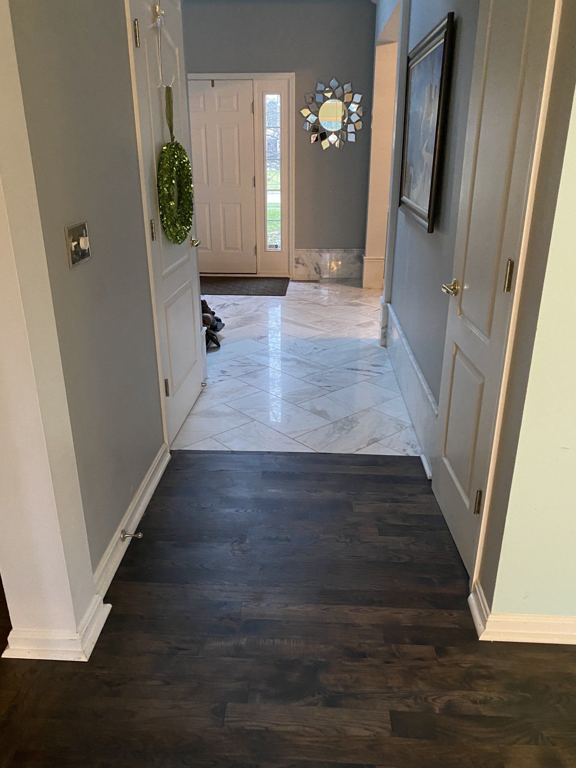 Hallway with dark wood floor leading to a bright entryway, gray walls, and a wall mirror.