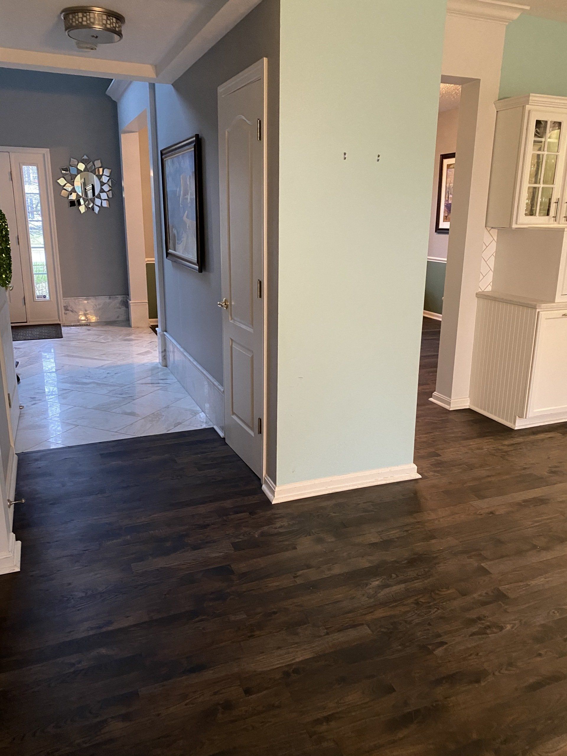 Hallway with dark wood floor, light walls, and a view into a tiled entryway and adjoining rooms.