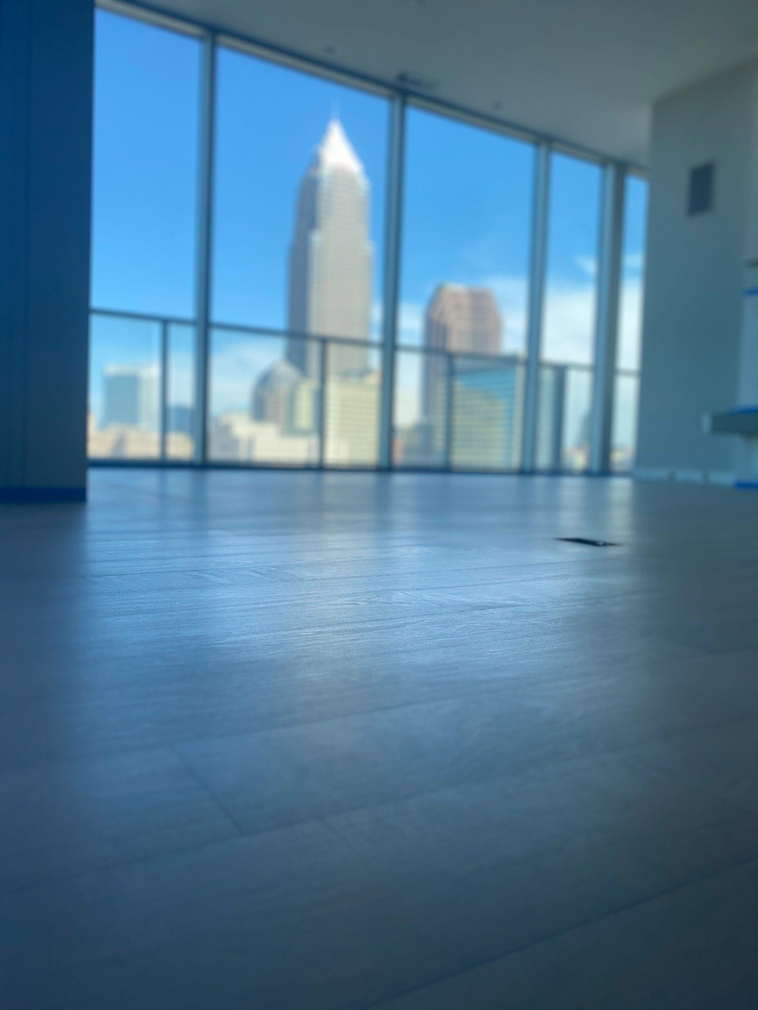 Empty modern room with floor-to-ceiling windows overlooking city skyscrapers and blue sky