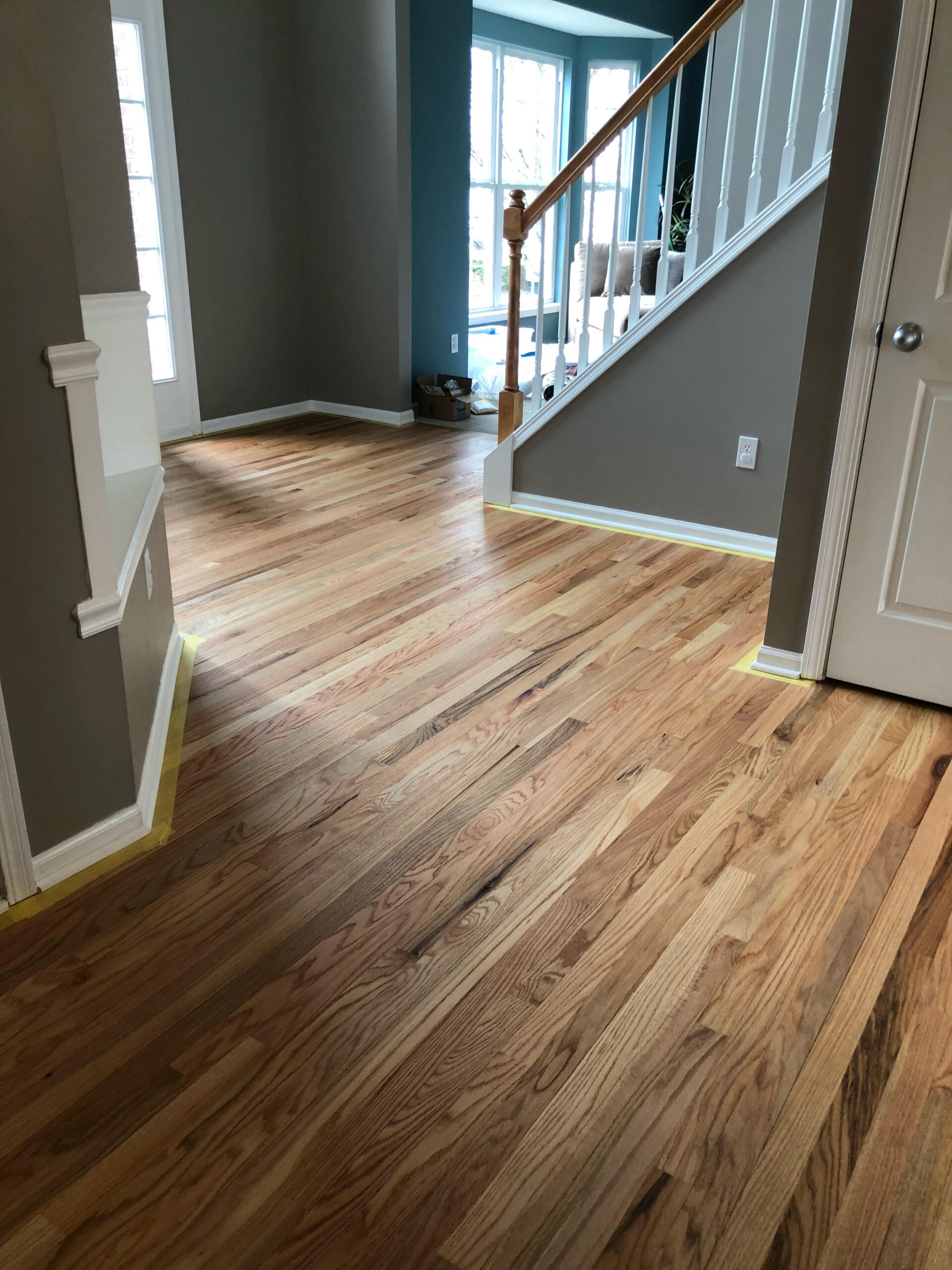 Hallway with light wood flooring, gray walls, white trim, and a staircase with white balusters.