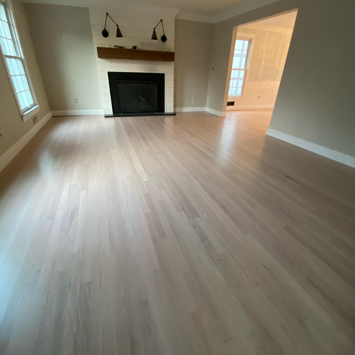 Empty living room with light wood floors, beige walls, fireplace, and wall sconces
