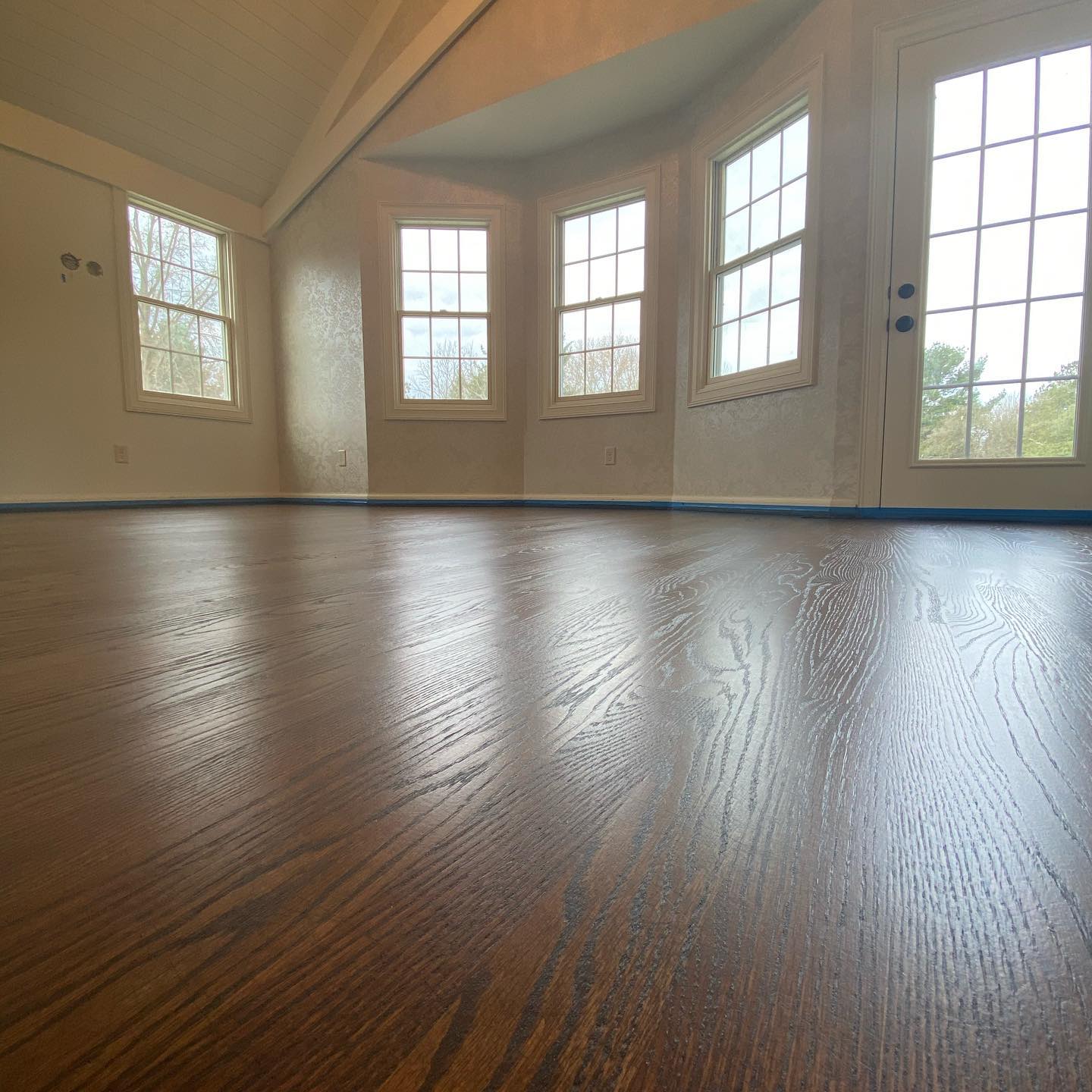 Empty room with dark hardwood floors, cream walls, and tall windows letting in daylight