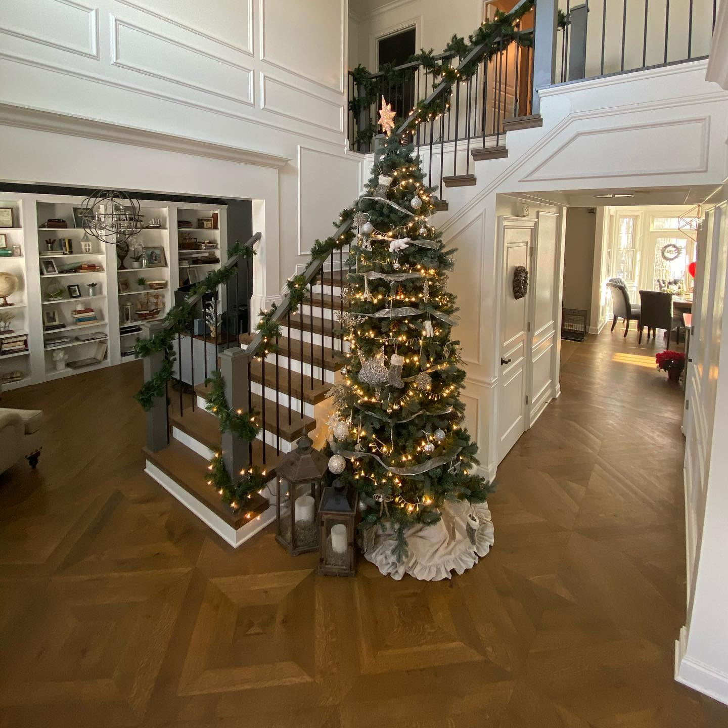 Festive foyer with a decorated Christmas tree beside a garlanded staircase and lanterns on wood floors