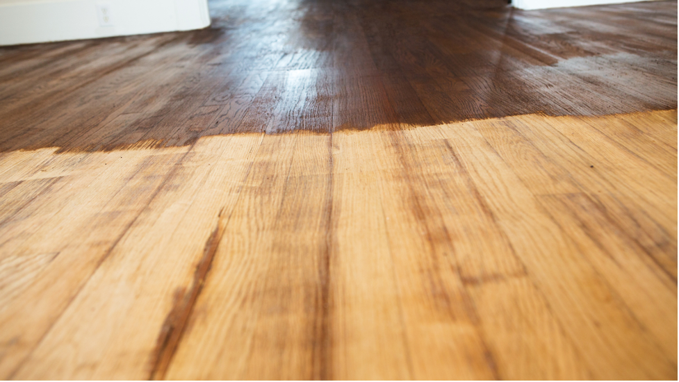 Close-up of a wooden floor with sunlight reflecting on the planks and a darker wood area in the background