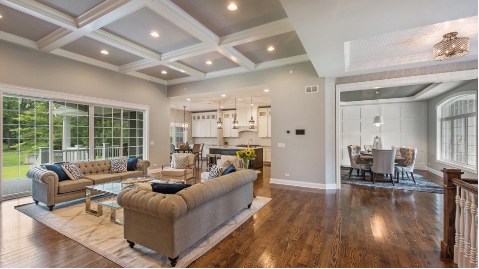 Spacious modern living room with gray sectional, coffered ceiling, hardwood floors, and open kitchen view