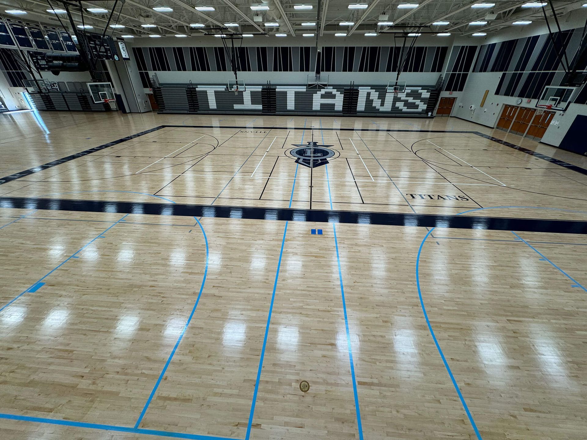 Empty indoor basketball court with polished wood floor and large “TITANS” lettering on the far wall
