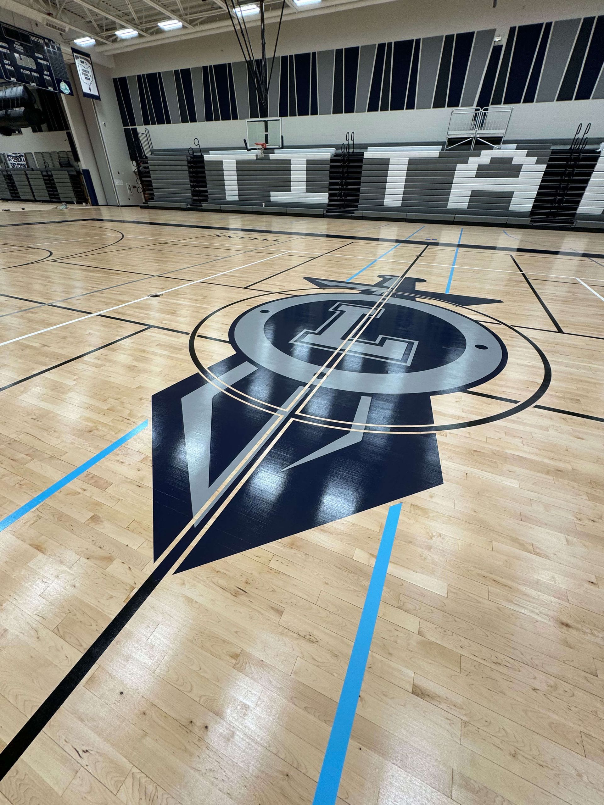 Empty indoor basketball court with polished wood floor and large center-court logo.