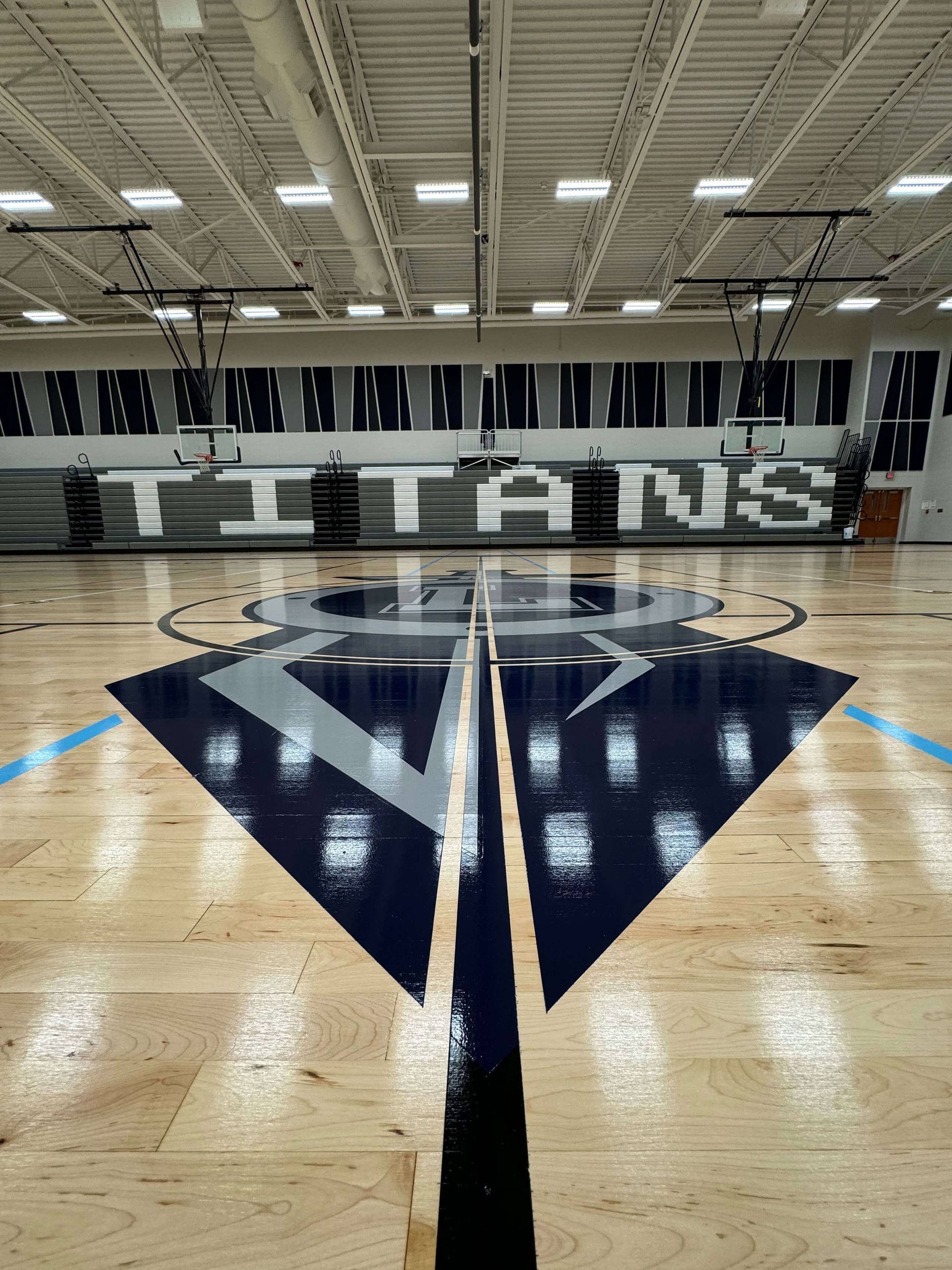 Empty indoor basketball court with a large center logo and bleachers reading “ST. JOHN’S”