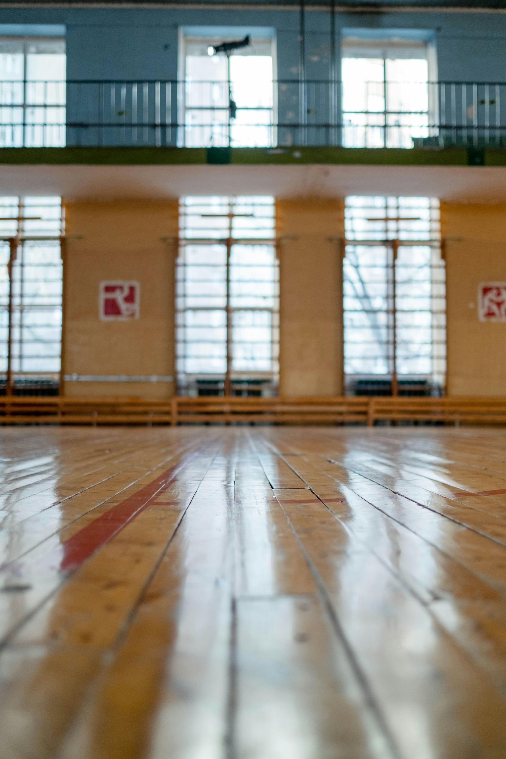 Empty indoor gym with polished wooden floor, large windows, and wall bars.