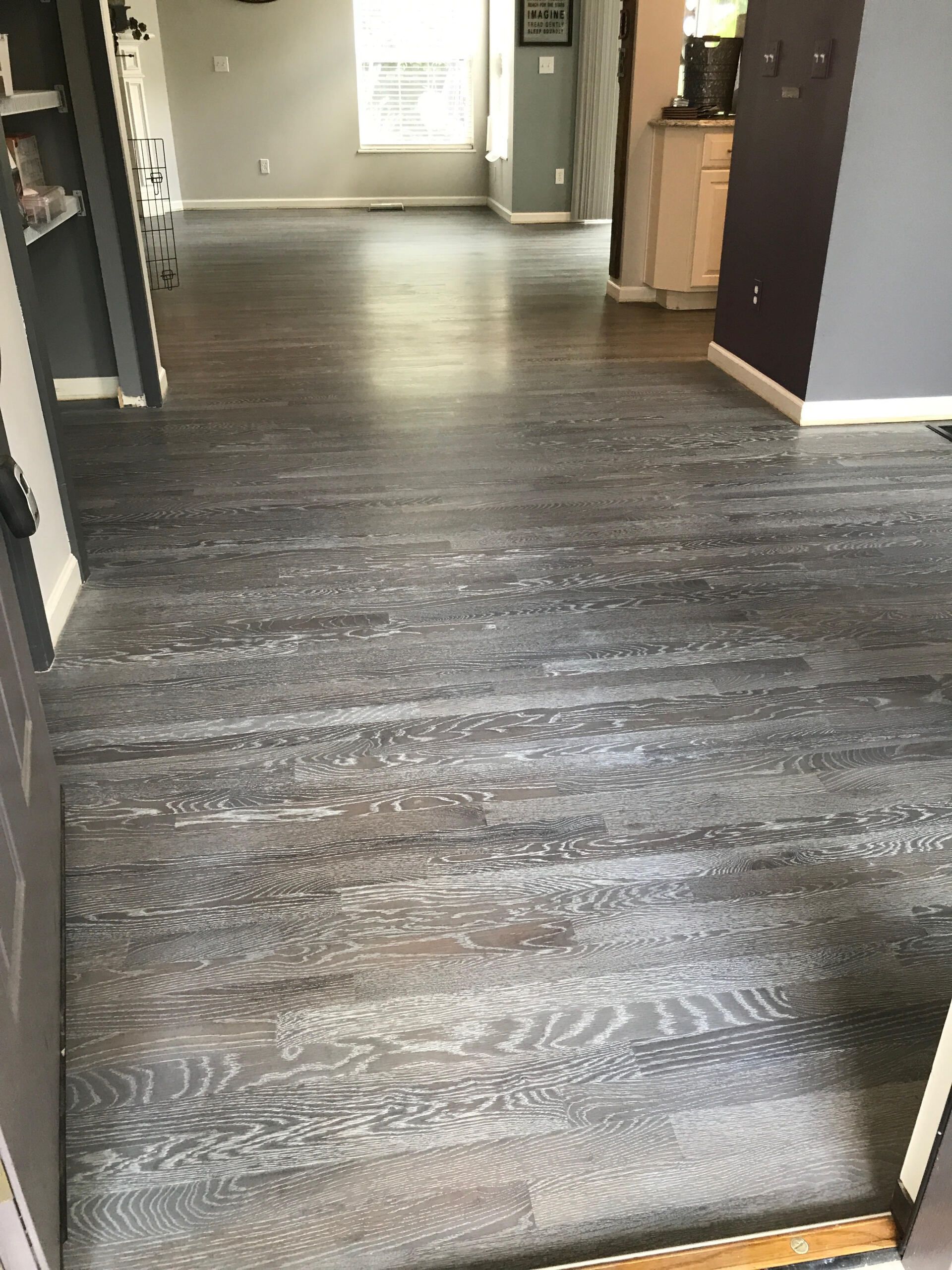 Empty hallway with dark wood flooring and cabinets along the sides, viewed toward a lit back wall