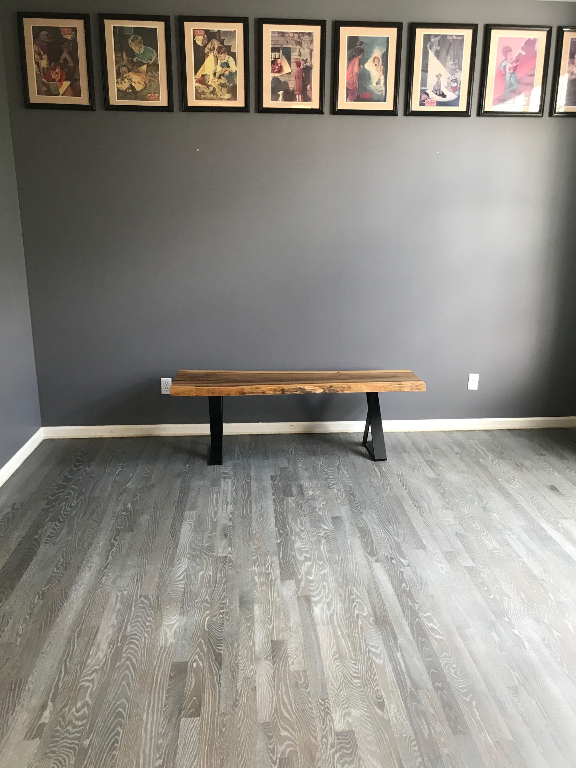 Empty room with dark gray walls, wood bench, framed art above, and gray patterned floor