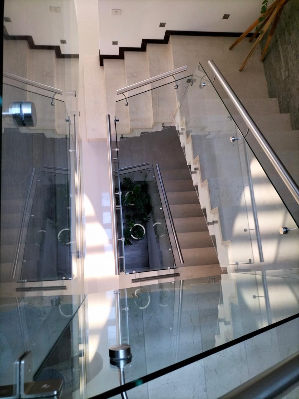 Vista aérea de una escalera moderna con barandillas de vidrio y escalones de color gris claro.