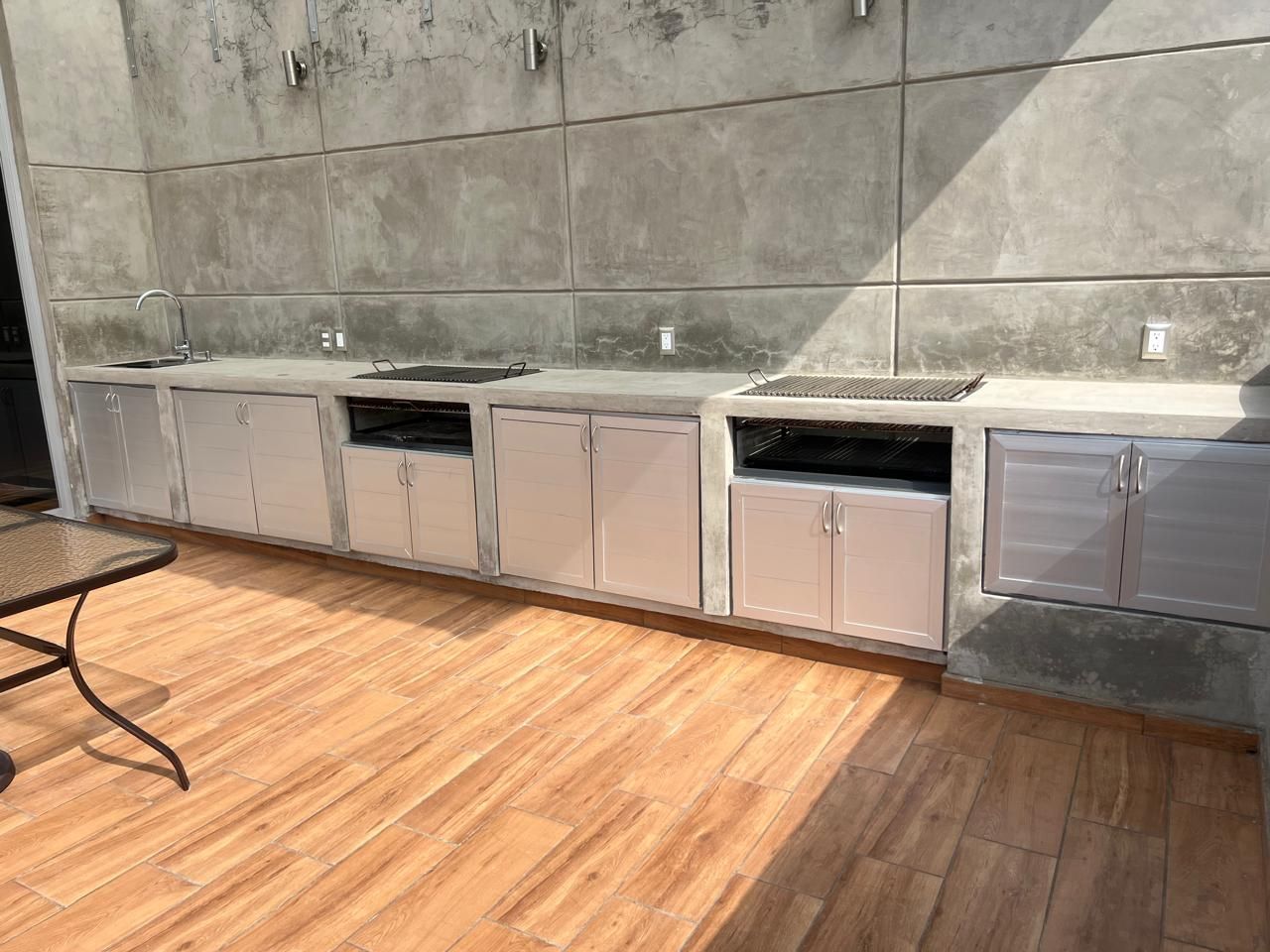 Cocina al aire libre con gabinetes de acero inoxidable y parrilla colocada contra una pared de concreto.