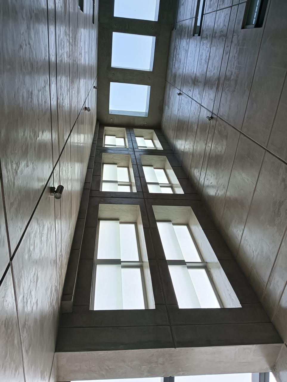 Espacio largo, alto y con ventanas en un edificio con paredes de hormigón y tragaluces cuadrados.