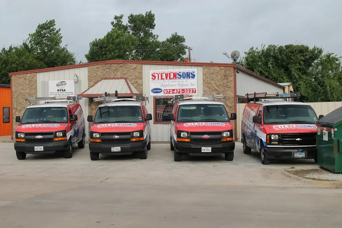 Four red service vans parked in front of a stone-faced building with the