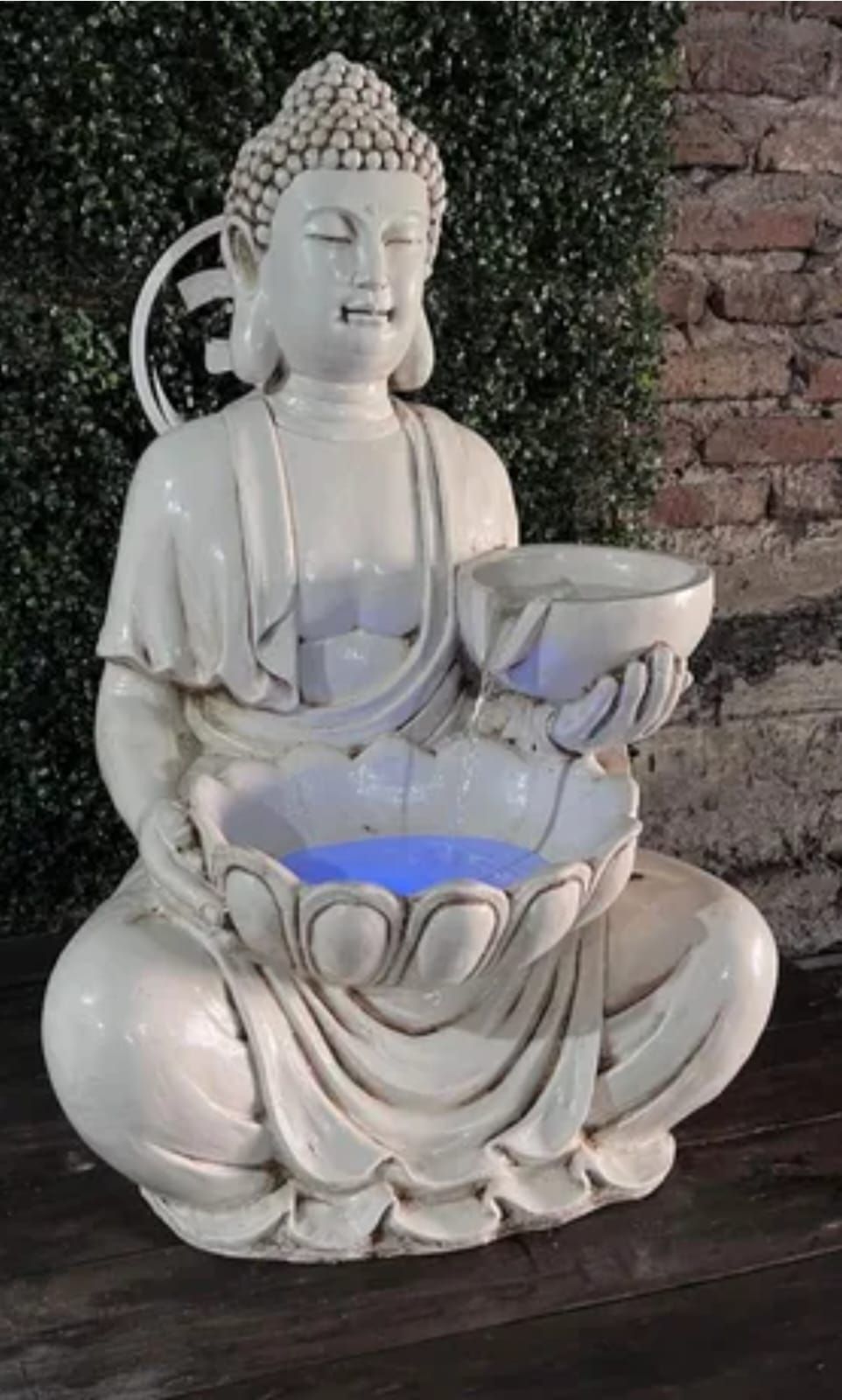 Estatua de Buda de plata sosteniendo un cuenco, sentada sobre una base de loto con una flor de loto iluminada en azul debajo.